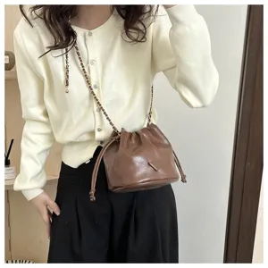 Chic brown leather bucket bag with chain strap and stylish triangular plaque design for women.