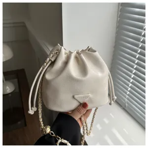 Detailed shot of white faux leather bucket bag with chain strap and drawstring closure.