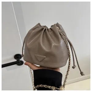 Detail shot of taupe PU leather bucket bag with chain strap and fashionable drawstring closure.