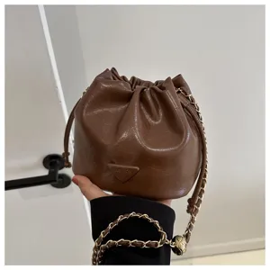 Brown bucket bag detail showing PU leather texture, chic chain strap and front triangle badge.