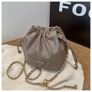 Chic taupe bucket bag with drawstring closure, stylish chain strap and trendy triangle patch.