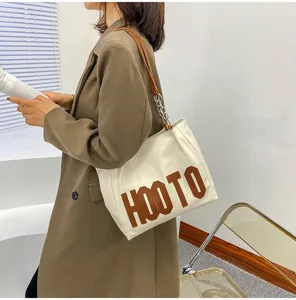Detailed view of women's beige tote shoulder bag with brown letter print and chic chain strap.
