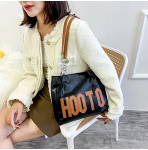 Detailed view of the black tote shoulder bag with brown straps and large letter print.