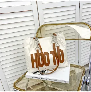 Detailed view of large white canvas tote bag with brown letter patch and chain strap.