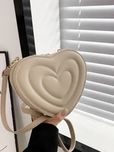 Close-up of a stylish beige heart-shaped quilted shoulder bag with chic gold hardware details.