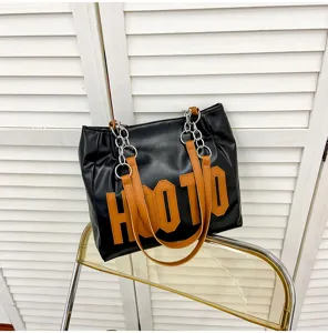 Detail view of a black tote bag featuring brown letter print, chain straps, and large capacity.