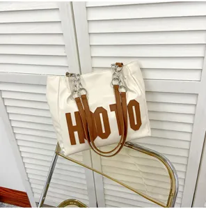 Detail view of the stylish white tote bag with brown letter details and chic chain handles.