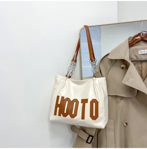 Detailed view of the white leather tote bag with brown letter print and chic chain strap design.