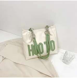 Detail shot of a stylish beige tote bag with green letter print, chain straps and large capacity.