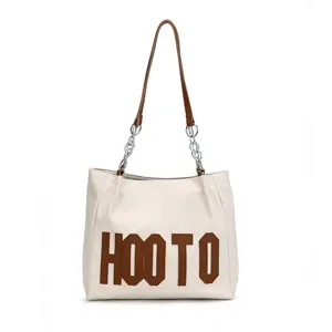Detail shot of white PU leather shoulder tote bag with chain strap and bold lettering.