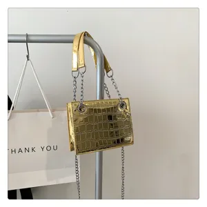 Gold metallic croc-embossed small shoulder bag detail with chain straps hanging on rack.