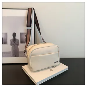 Detail view of white PU leather crossbody bag, featuring wide striped strap and chic metal plate.