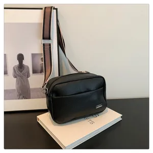 Close-up of black PU leather crossbody bag with wide striped strap and metal detail.