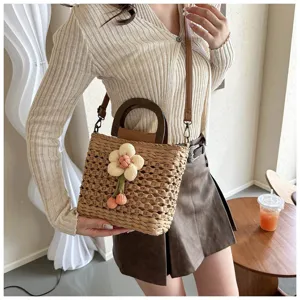 Chic straw woven bucket bag with wooden handle and floral charm for stylish summer casual wear.