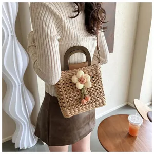 Detail shot of stylish straw woven handbag with wooden handle and cute plush flower pendant.