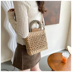 Detail shot of a casual woven straw bag with wood handle and leather strap on model.