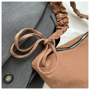 Brown canvas shoulder dumpling bag detail, stylish pleated strap and zipper closure.