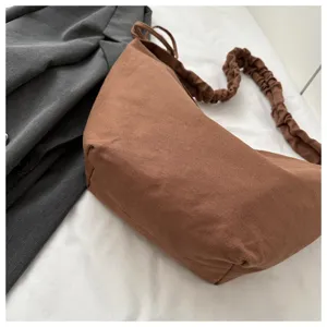 Detail shot of a brown canvas dumpling shoulder bag with ruched strap displayed on white.