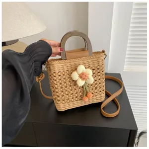 Detail view of stylish straw woven handbag with wooden handle and cute plush flower.