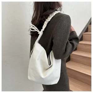 Detail shot of a casual white canvas shoulder bag featuring pleated straps and bow ties.