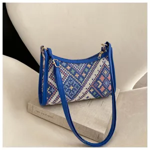 Close-up view of ethnic geometric woven shoulder bag with blue leather strap on book prop.
