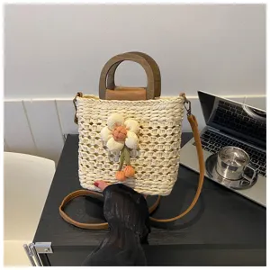 Detailed view of stylish straw bucket bag with wooden handle and flower decor on table.