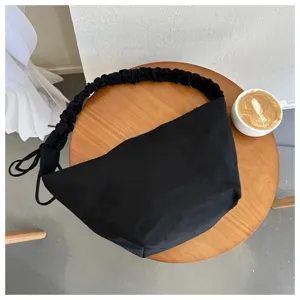 Detailed view of the black canvas pleated shoulder bag on a wooden table with a coffee cup.
