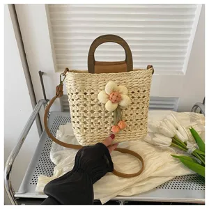 Detailed view of the woven straw bucket bag featuring a wooden handle, fabric flower, and strap.