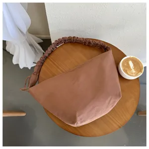 Detailed view of a brown canvas dumpling shoulder bag with scrunchie strap on wooden table.