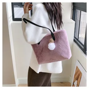 Detail view of a stylish pink plush shoulder bag with a fluffy pom-pom charm and black strap.