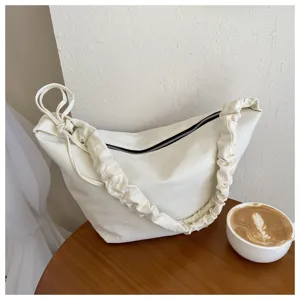 Minimalist white canvas shoulder bag detail shot, featuring unique pleated strap and smooth zipper.