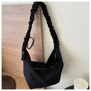 Detail shot of the black canvas shoulder bag showing its unique pleated strap and zipper design.