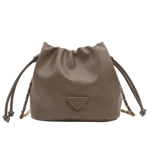 Brown leather bucket bag detail showing drawstring closure, metal chain, and fashion front patch.