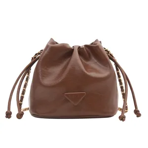 Brown leather bucket bag detail view, stylish shoulder bag with chain strap and drawstring.