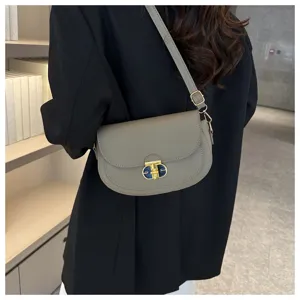 Detailed view of stylish grey leather shoulder bag with metallic turn-lock closure on model.