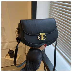 Close-up detail of black leather saddle shoulder bag with golden lock design and strap.