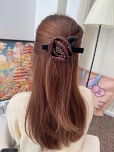 Detail view of a retro brown polka dot fabric rose rhinestone hair clip worn on back hair.