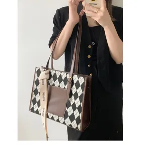 Close-up detail of stylish argyle tote bag with brown leather pocket and chic ribbon accent.