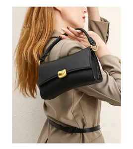Close-up of stylish black leather baguette shoulder bag worn by model, metallic gold clasp.