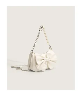White shoulder bag detail showing pearl chain strap, metal heart link and elegant front bow.
