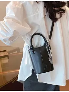 Detail shot of a sleek black bucket bag with a chic pearl leaf pendant and sturdy handle.
