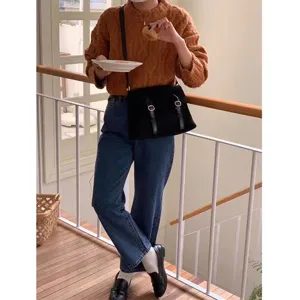 Detailed view of retro suede crossbody messenger bag worn with knit sweater and denim.