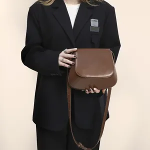 Detail view of brown PU leather saddle bag, elegant shoulder strap and smooth curved design.