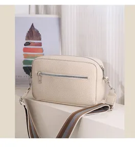 Detailed shot of a beige PU leather crossbody bag with a wide striped strap and zipper.