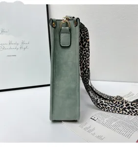 Close-up detail view of a sage green suede bucket bag featuring a chic leopard print wide strap.