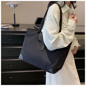 Detail view of a black commuter tote bag with leather corner guards worn on shoulder.