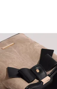 Close-up view showing the canvas texture and elegant black leather bow on the handbag.