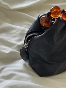 Detailed shot of black textured leather handbag with amber beaded handle, elegant design.