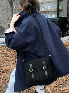 Detail view of a vintage black suede messenger bag, retro crossbody satchel with dual buckles.