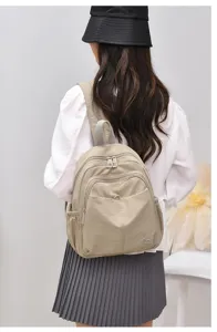 Detail shot of beige nylon casual backpack worn by model, showing multi-pocket design and strap.